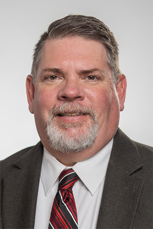 Headshot of James Graham, a white male wearing a brown suit coat, white dress shirt and red and white striped tie. He has brown hair and a partially grey goatee.