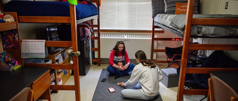 Two students play a game on the floor of their room in Grimm hall. Both beds are lofted with furniture underneath