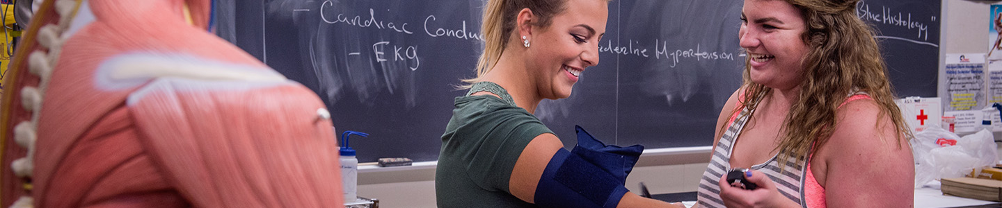 One student puts a blood pressure monitor on the arm of another student during a physiology class