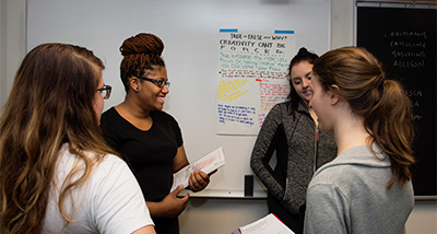 Four Sociology students review notes in front of a whiteboard