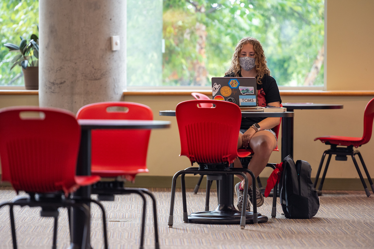 A student wearing a face covering during COVID-19 does homework in the Involvement Center