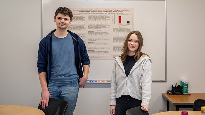 Justin Gasparas and Desirea Laurie-Szabla stand in front of a whiteboard and poster with their research results on it.