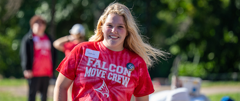 A student smiles at the camera wearing a red Falcon Move Crew volunteer t-shirt
