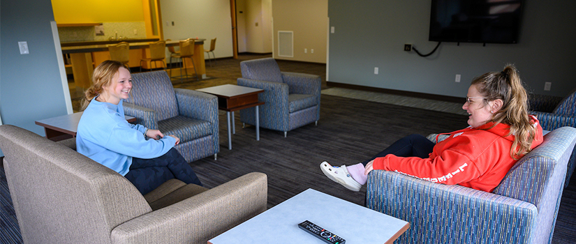 Ames pod full living room including seating, a television, tables, and two students talking