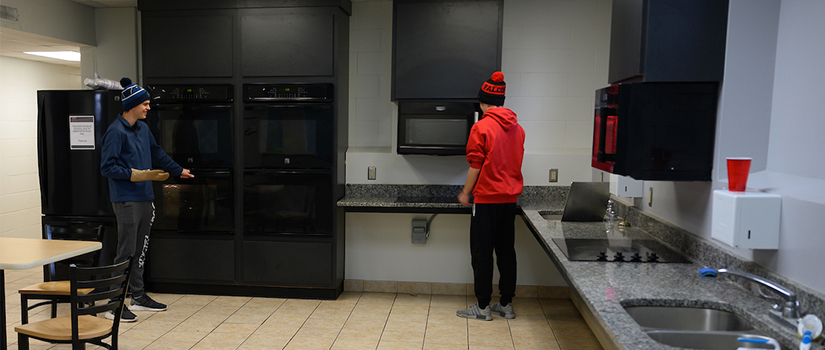 Two students use the spacious kitchen in Crabtree hall. With four ovens, two ranges, two sinks, two microwaves, and considerable counterspace, students have space to spread out.