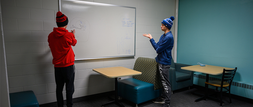 Two students use a study room in the basement of Crabtree hall, which provides seating and a whiteboard.
