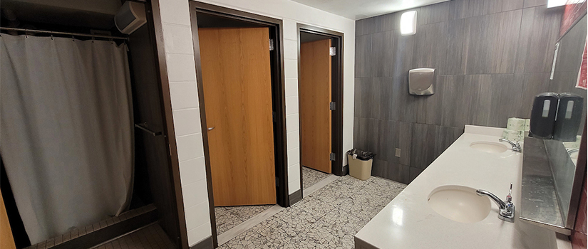 A bathroom in Grimm hall includes private shower stalls and shower stalls, with two sinks side-by-side. Mirrors, outlets, and hand dryers are available.