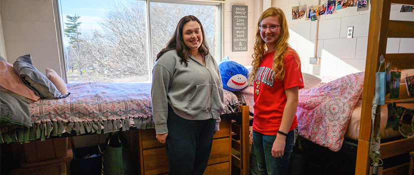 Roommates within Johnson Hall stand in front of their beds.