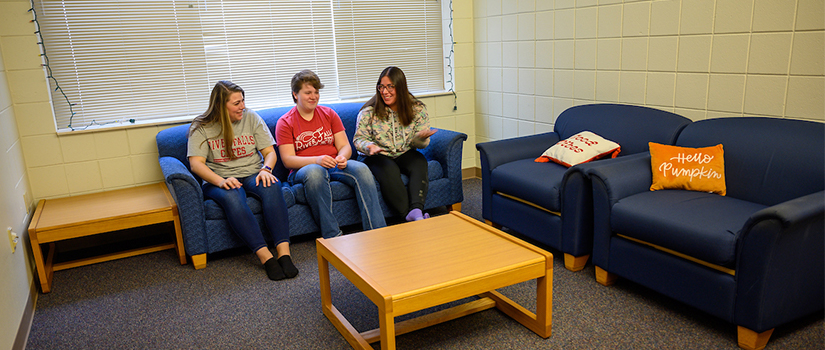 South Fork Suites living room with seating, tables, and three students talking