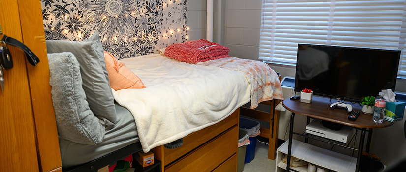 A room in May hall showing a bed, edge of a desk, and a student's television.