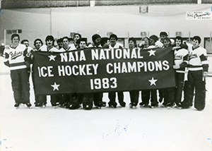 a black and white photo of a hockey team holding a large banner that says NAIA National Ice Hockey CHampions 1983