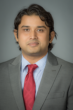Rahul Gomes headshot. Male with brown hair wearing a grey suitcoat and red tie