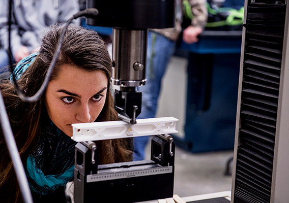 Student watches a 3D printed beam in a stress test machine