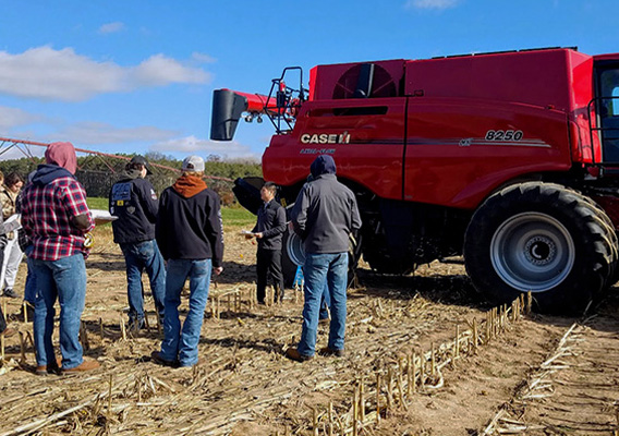 Agricultural Studies class stand in a field around a combine
