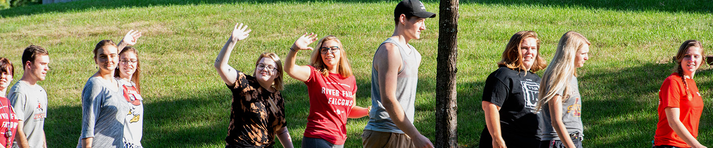 Three students wave to camera as they walk by