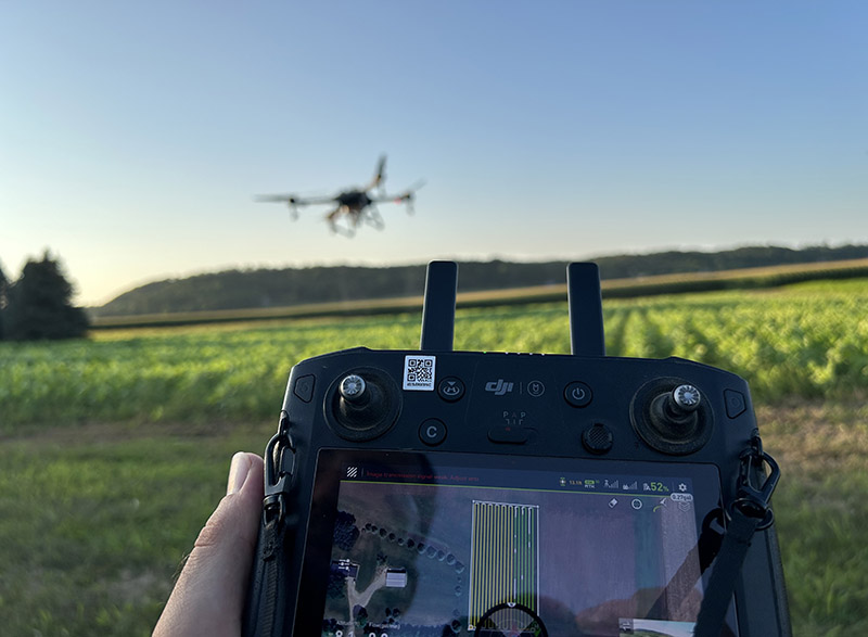 a remote control controls a drone flying over a field 
