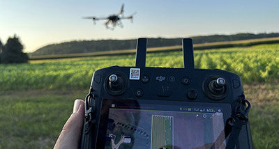 a remote control controls a drone flying over a field 