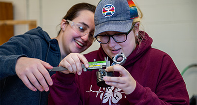 Two Students measuring an engine part with a caliper