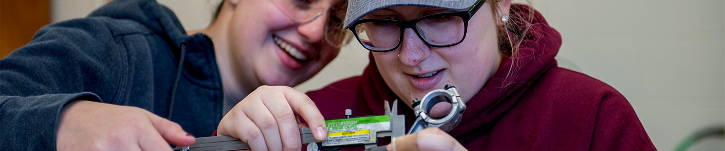 Two Students measuring an engine part with a caliper