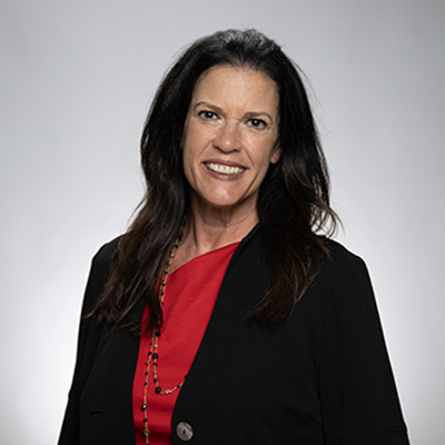 Amy Clark head shot. A woman with long dark hair wearing a red blouse and black blazer in front of a grey background