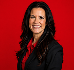 Amy Clark head shot. A woman with long dark hair wearing a red blouse and black blazer in front of a red background
