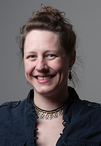 Arriety Lowell headshot. A woman with brunette hair in a bun wears a blue top and a decorative necklace.