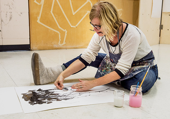 Art student paints on canvas while sitting on the floor