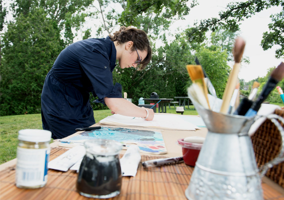 Art student paints on canvas outside on a picnic table