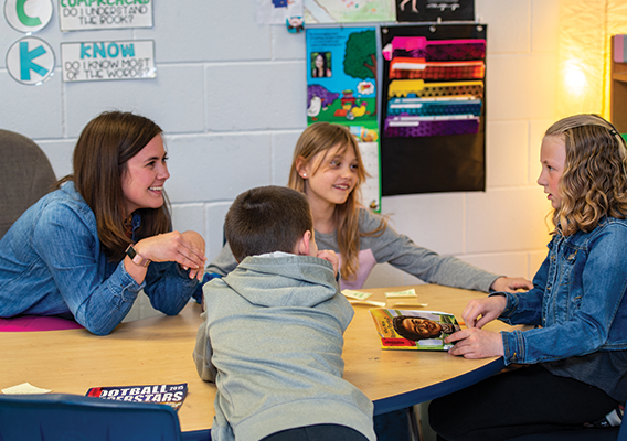 teacher at table of students discussing a book