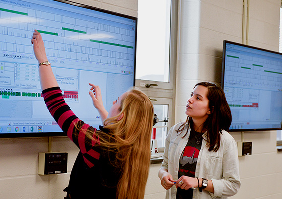 Two Biotechnology students analyze information on a TV screen