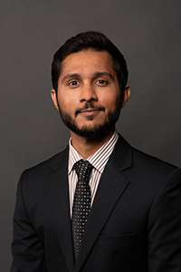 Shaheer Burney Headshot. A man with dark hair and black facial hair wears a black suit jacket and polka dotted tie.