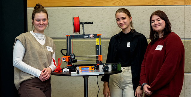 Three students pose with a 3D printer during the URSCA gala