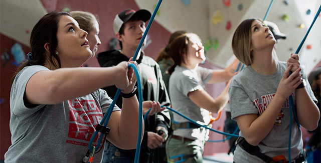 Multiple students climb the wall in the Falcon Center