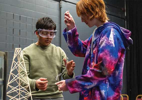 two young men work together on a science experiment with string and wooden pieces