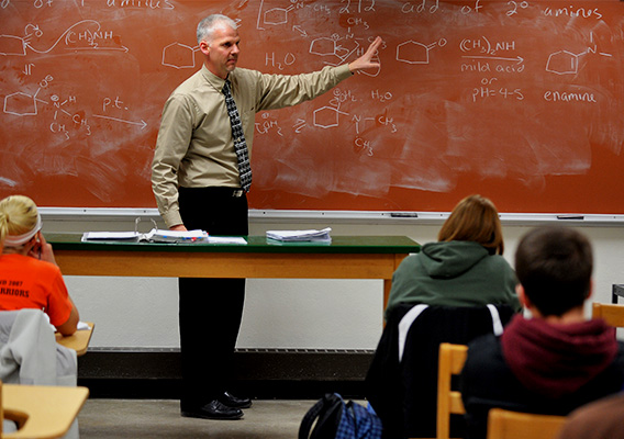 Chemistry professor speaks to students in front of a chalkboard