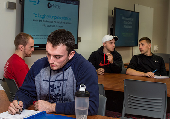 Student takes notes during class as others ask questions