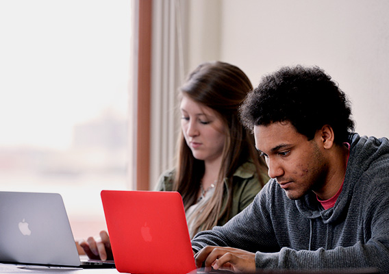 Two students type notes on their laptops during class