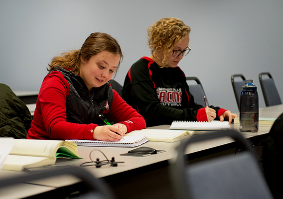 Two students take notes in a notebook during class