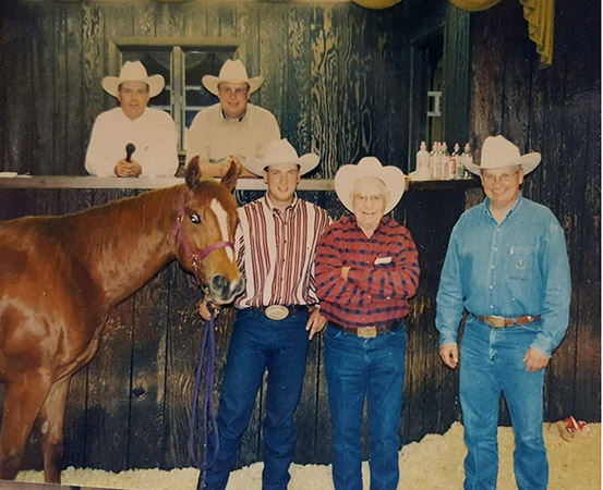 Five men wearing white cowboy hats pose with a horse