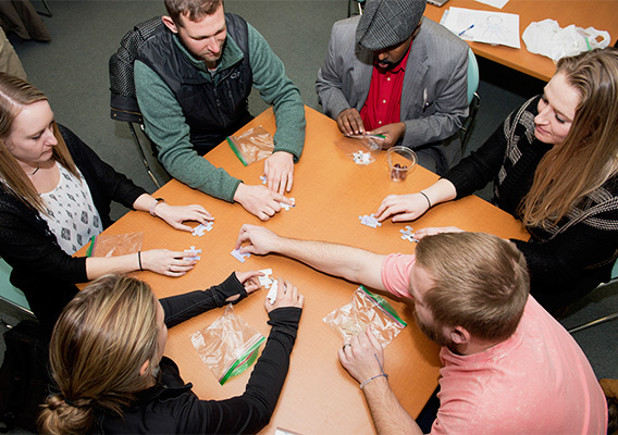 Group of Counseling graduate students sit at a round table putting together a puzzle