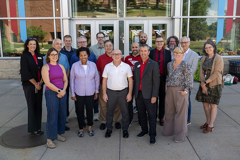 The Faculty Senate gathers together for a group photo. There are 17 people, a mix of males and females, all wearing business causal clothing.