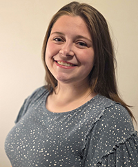 Delani Dow headshot. A college age woman with shoulder length brunette hair