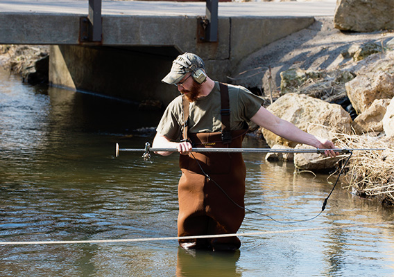 Environmental Engineering student takes a water sample out of the KinnicKinnic River