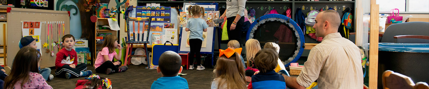 Two student teachers sit among a group of preschoolers in a classroom