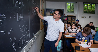 Economics professor writes equations on chalkboard during class