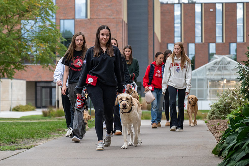 a group of female students walk alongside their new assistance dogs in training on the UWRF campus