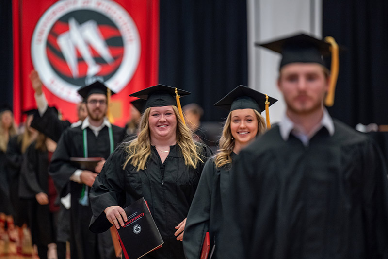 students wearing commencement regalia march across the graduation stage