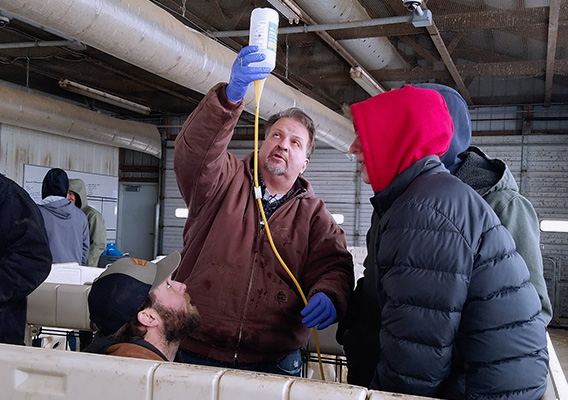 A professor hold a bottle and tube in the air so liquid can drip down