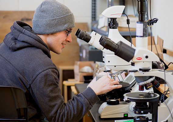 A geology student studies rocks under a microscope