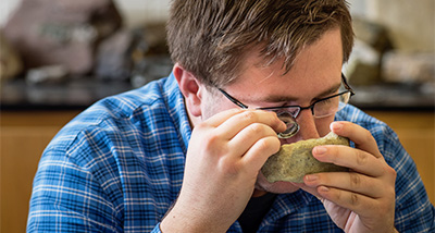 Geology student viewing a fossil with a small handheld magnifying glass